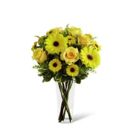 Tall clear vase of yellow roses and gerbera daisies
