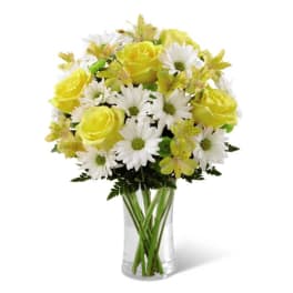 Yellow roses, white daisies, and yellow alstroemeria in a clear glass vase