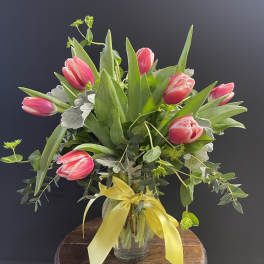 Pink tulips in a glass vase with a yellow ribbon