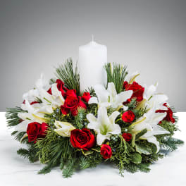 Low centerpiece of white lilies and red roses with evergreens around a white pillar candle