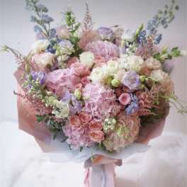 Large pastel bouquet of pink, white, and blue flowers wrapped in pink paper