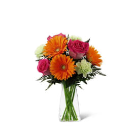 Bright bouquet of orange gerbera daisies, pink roses, and green carnations in a clear glass vase