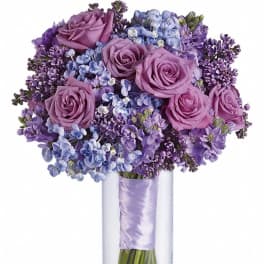 Lavender roses and light blue hydrangeas in a tall clear glass vase with a satin-wrapped stem bundle