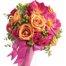 Hand-tied bouquet of orange roses and bright pink flowers wrapped in pink ribbon in a clear glass vase