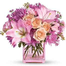Pink lilies, peach roses, and lavender mums arranged in a pink glass cube vase