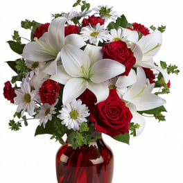 Arrangement of white lilies, red roses, red carnations and white daisies in a red glass vase