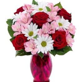 Arrangement of red roses, white daisies, and pink alstroemeria in a bright pink glass vase