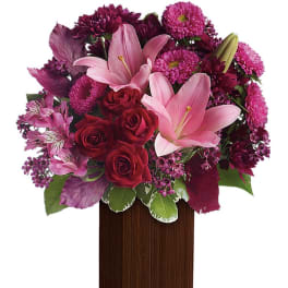 Tall arrangement of pink lilies, red roses and purple flowers in a dark rectangular wooden vase