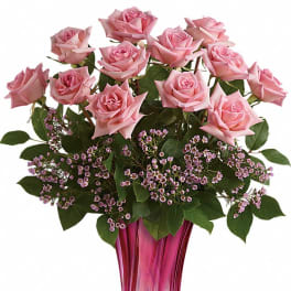 Pink rose arrangement with tiny pink filler flowers in a tall pink glass vase