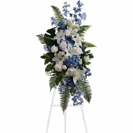 Tall standing spray of white lilies and roses with blue flowers on a white easel
