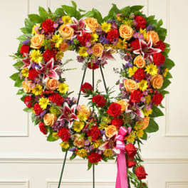 Heart-shaped standing wreath of bright mixed flowers with a pink ribbon and cascading roses