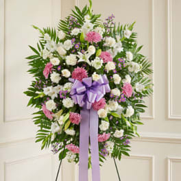 Standing spray of white lilies and carnations with pink mums and a lavender bow on an easel