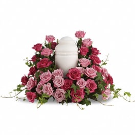 Cremation urn encircled by pink and dark pink roses with trailing ivy.