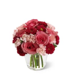 Short arrangement of pink roses, pale carnations, and red mums in a clear glass vase