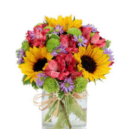 Bright mixed bouquet with sunflowers, pink blooms, and green accents in a glass jar vase