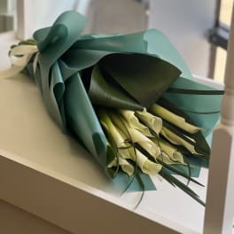 Bouquet of white calla lilies wrapped in teal paper