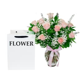 Pink rose bouquet in a glass vase with a ribbon, beside a white flower gift bag