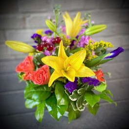 Bright mixed bouquet with yellow lilies, coral roses, and purple accents in a vase