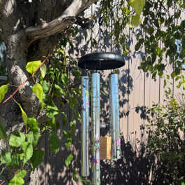 Hanging wind chime with silver tubes and a black top in a garden