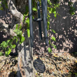 Black metal wind chime with Amazing Grace inscription hanging from a tree outdoors