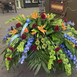 Large floral spray with orange lilies, blue flowers, and burgundy carnations