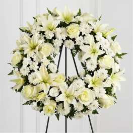 White floral wreath on a black stand with roses and lilies