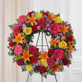 Large circular funeral wreath with roses, lilies, and daisies on an easel