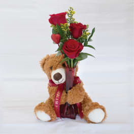 Teddy bear holding a vase of red roses with a heart pick
