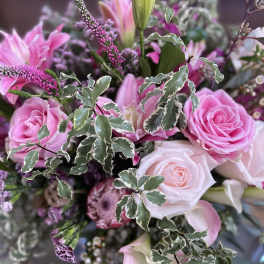 Pink roses and lilies arranged with variegated foliage.