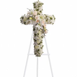 Tall white floral cross with lilies and pale roses on a stand