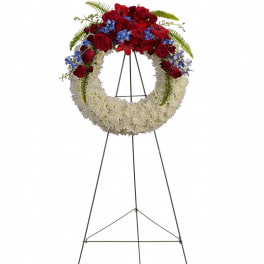 Standing wreath of white flowers with red roses and blue blooms on a metal easel