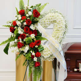 Standing funeral spray with red roses and white flowers beside a casket