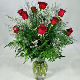 Red roses arranged in a clear glass vase with airy greenery