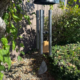 Black memorial wind chime hanging outdoors among trees and shrubs
