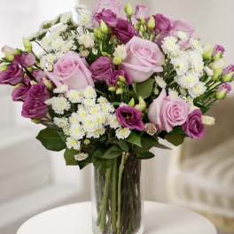Bouquet of pink and purple roses with white daisy flowers in a glass vase