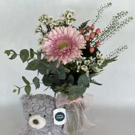 Pink gerbera bouquet in a glass vase with a gray teddy bear