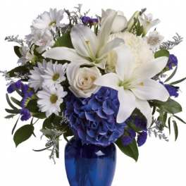 White lilies and daisies with blue hydrangea in a cobalt vase