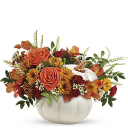 Low fall arrangement of orange roses and mixed blooms in a white pumpkin container