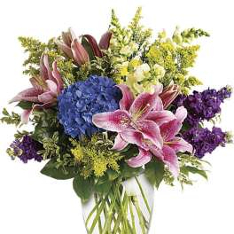 Bouquet of pink lilies, blue hydrangea, and purple flowers in a glass vase