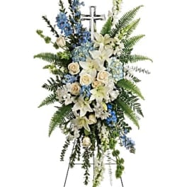 Standing floral spray with white lilies, blue flowers, and a cross