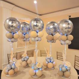 Silver balloons on stands with small cream floral accents on a table