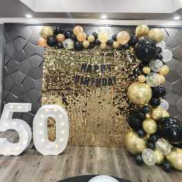 Birthday backdrop with gold and black balloons and large lit number 50