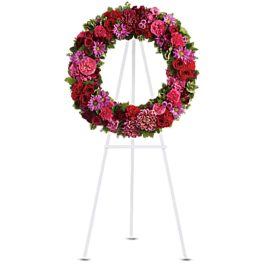 Circular floral wreath on a white easel stand with pink, red, and purple flowers