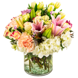 Mixed bouquet of pink lilies, roses, hydrangeas, and tulips in a glass vase