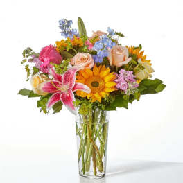 Mixed bouquet with roses, lilies, and a sunflower in a clear glass vase