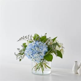 Blue hydrangea bouquet in a clear glass vase with white accent flowers