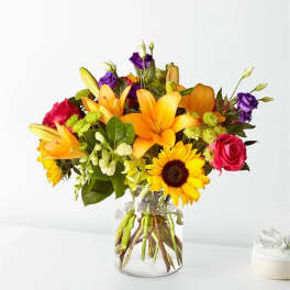Mixed bouquet of lilies, roses, and sunflowers in a glass vase