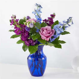 Mixed bouquet of pink, purple, and blue flowers in a cobalt blue vase