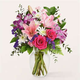Mixed bouquet of pink lilies, roses, and purple flowers in a glass vase
