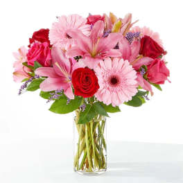 Pink lilies, roses, and gerbera daisies in a clear glass vase